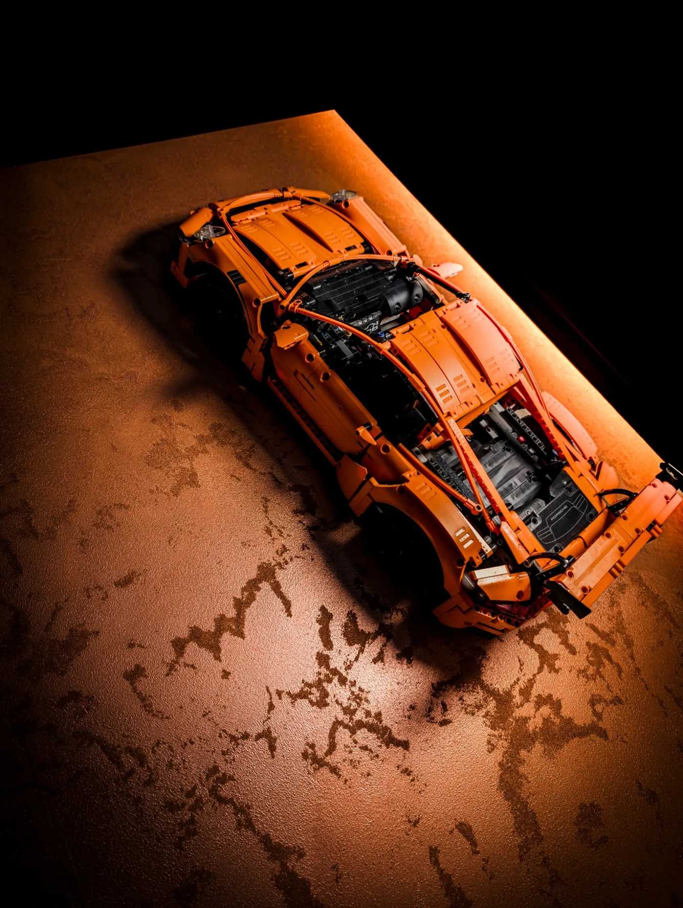 Orange model car displayed against a warm metallic-effect surface