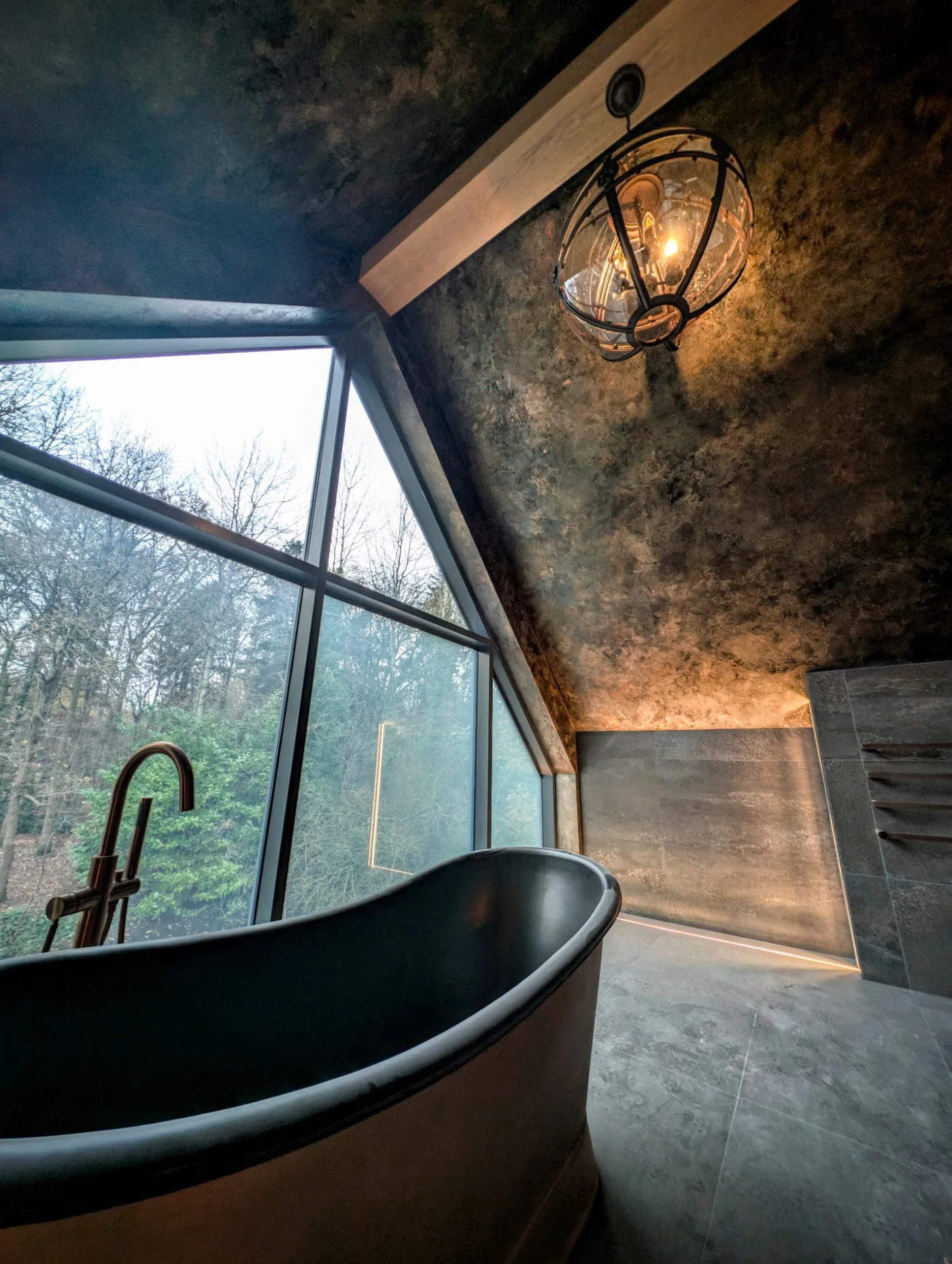 Dark freestanding bath below a sloping decorative ceiling